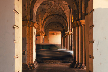 Fototapeta premium Blurred car passing under stone arches, symbolizing fast urban life, transportation, and contrast between motion and historic architecture.