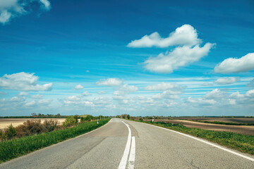 Naklejka premium Open country road under blue sky with white clouds stretching across flat landscape