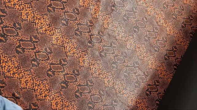 An exotic orange and black snakeskin faux leather material features a textured reptile scale finish and a black felt backing for fashion apparel handbags and upholstery design
