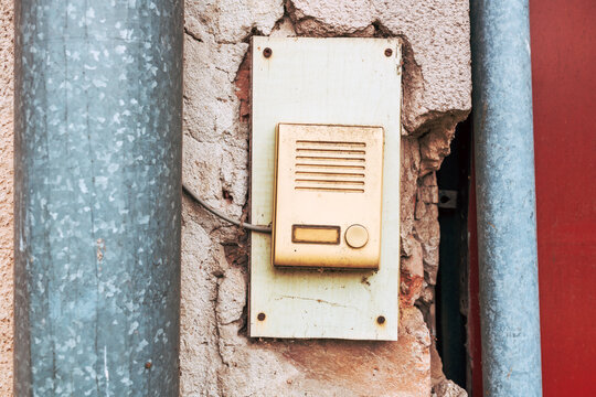 Vintage doorbell intercom on cracked plaster wall between metal pipes at old building entrance