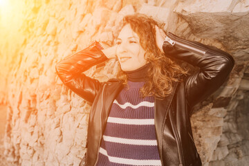 Obraz premium Woman leather jacket portrait posing against stone wall in bright sunlight for fashion and lifestyle concepts