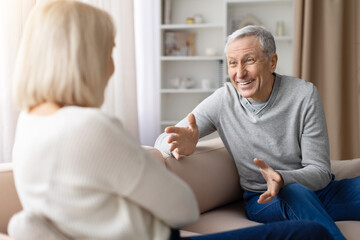 Obraz premium Emotional senior man gesturing during conversation with mature woman at home, expressing strong feelings in domestic relationship discussion scene