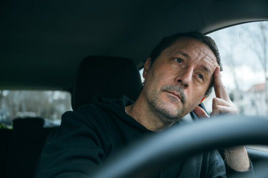 Unhappy male driver resting with hand on face inside vehicle, contemplative mood and everyday exhaustion concept