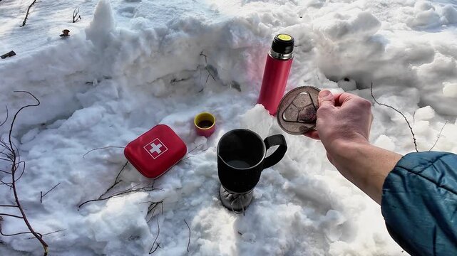 Thermos And Mug On Snow, Red Medical Case And Filter Beside Black Mug, Hand Pouring Hot Water Into Strainer, Cozy Survival Preparation On Winter Site With Jacket Sleeve And Steaming Steam