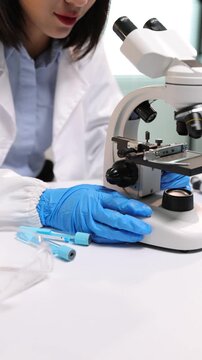Scientist wearing gloves and lab coat working in a modern laboratory. Medical researcher using professional microscope for analysis.