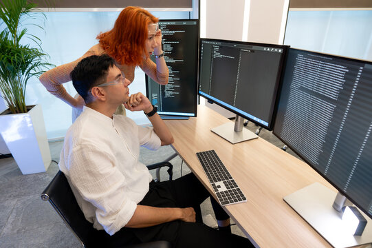 Two colleague discuss about data displayed on monitor, both engaged in a collaborative programming session in a well-lit office setting.