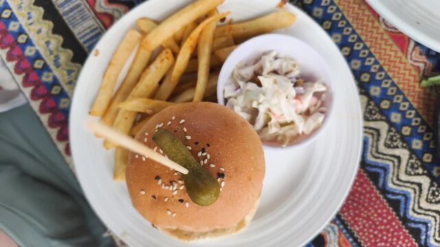 Beef burger with gherkin features juicy patty topped with small pickled cucumber on sesame bun. Golden french fries and creamy sauce complement beef burger with gherkin for hearty tasty meal.