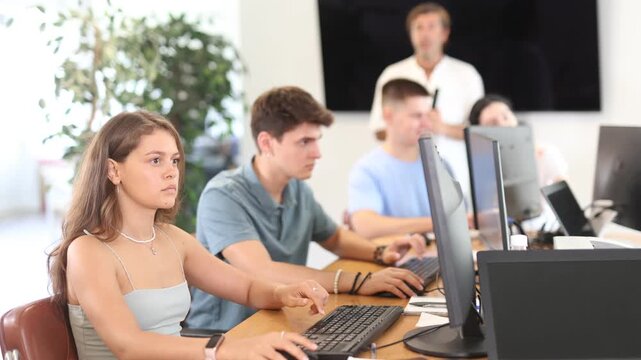 Positive interested young girl using computer to surf internet in busy library, searching educational resources and materials during self-study