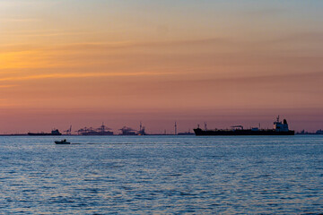 Obraz premium Cargo ship, small boat navigating industrial port sunset