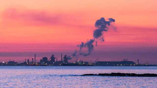 Industrial pollution creating smoke over water at sunset