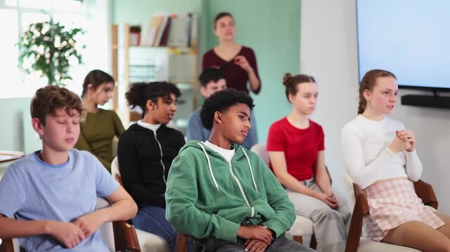 Focused group of diverse teens attending educational session with instructor speaking in school classroom