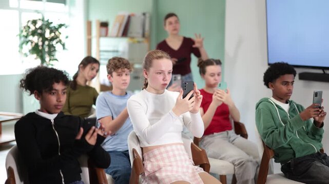 Attentive teenage students using smartphones to scan QR codes during lesson with teacher in background. High quality 4k footage