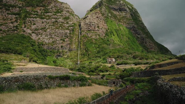 Panoramic View of a Majestic Waterfall Flowing Down Massive Lush Green Volcanic Cliffs into a Terraced Valley, Po&ccedil;o da Alagoinha, Flores Island, Azores