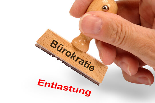 Ein Holzstempel ist beschriftet mit dem Aufdruck B&uuml;rokratie und dem Abdruck Entlastung