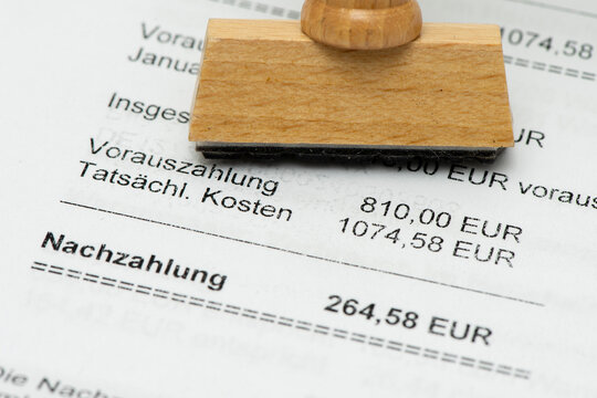Ein Holzstempel mit Freiraum f&uuml;r individuellen Text steht auf einer Nebenkostenabrechnung f&uuml;r eine Mietwohnung mit Berechnung des pers&ouml;nlichen Verbrauchs und einer Nachzahlung. - Symbolbild