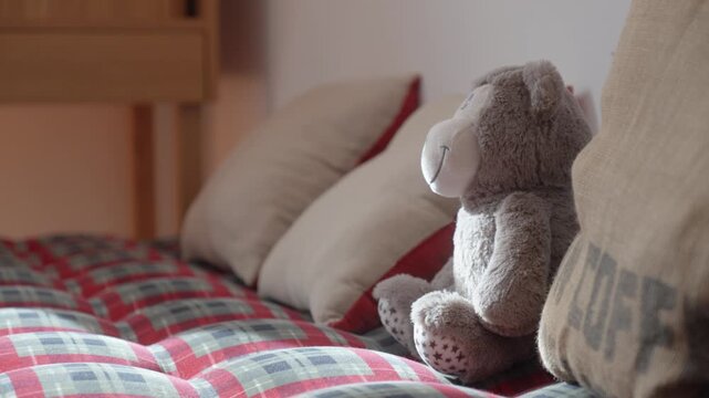 Teddy bear resting on red bed with pillows in cozy bedroom interior under soft natural light