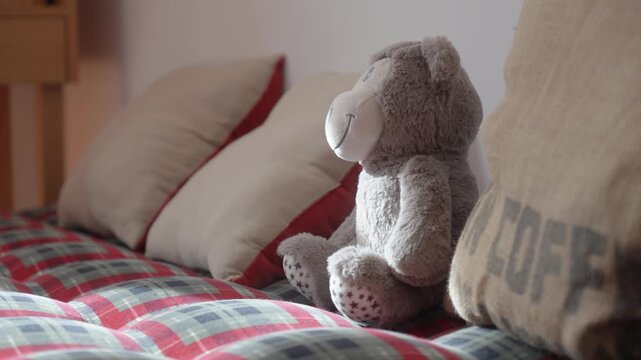 Teddy bear sitting on bed with decorative pillows in warm home interior setting