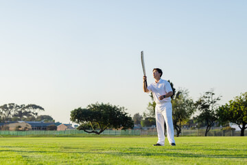 Obraz premium Male cricketer in whites standing on pitch holding bat, sporting wristband, looking up, copy space