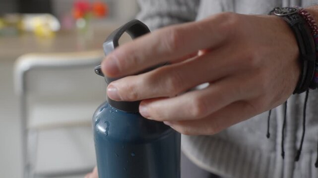 Hand tightening to close reusable water bottle cap in kitchen setting with soft natural indoor light
