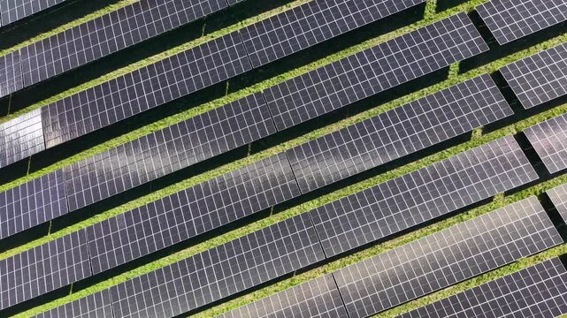 A tracking drone shot providing a top-down geometric perspective of sun-reflecting solar panels in a Danish countryside renewable energy facility.