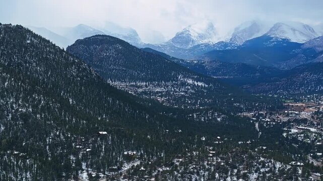 Estes Park mountain valley with dense forest and snow patches beneath cloudy sky, aerial drone overview