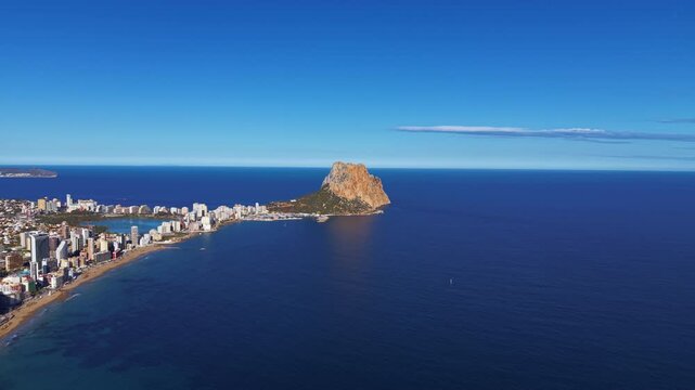 Calpe coastline in Spain featuring the iconic Penon de Ifach rock rising from the Mediterranean Sea alongside the city beach and marina under clear blue skies