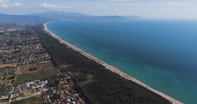 Aerial view of the long sandy coastline and turquoise Tyrrhenian Sea with lush pine forests and distant mountains in Paestum, Campania, Italy.