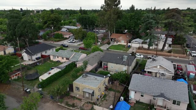 Residential neighborhood in Modesto, California with modest homes, narrow streets, parked cars and dense layout, everyday suburban living environment in Central Valley,United States. Aerial flyover.