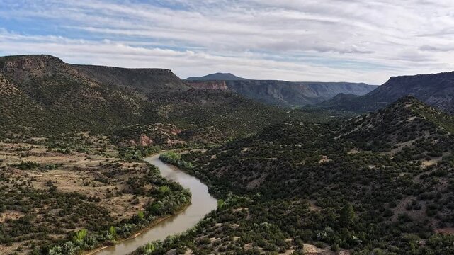4K timelapse captures the Rio Grande river winding through a lush green hidden canyon gorge. Cinematic aerial view features mesmerizing patches of light phasing through the southwestern landscape.