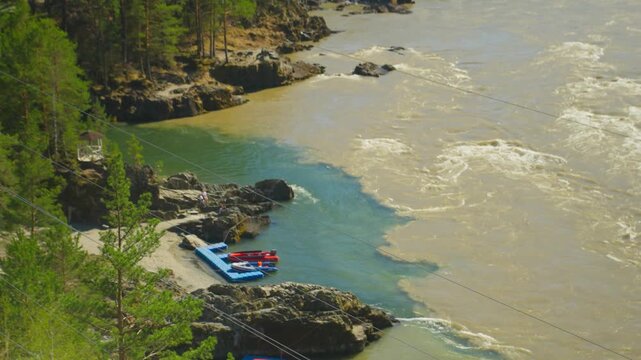 Aerial View Of Turquoise River Rapids With Blue Raft Docked On Rocky Shoreline, Pine Forest Framing Rugged Canyon, Powerful Current Meeting Calm Eddy, Sunlight Sparkling On Swirling Water, Cinematic