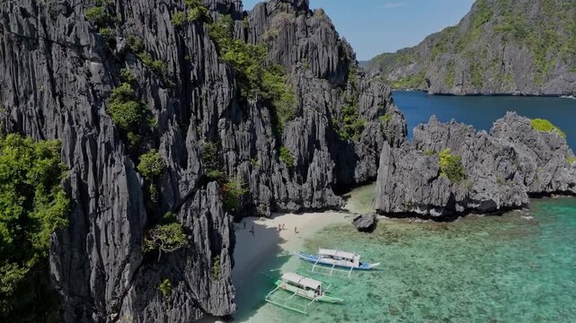 Dramatic drone flight moving backwards and upwards from a tropical beach to reveal the stunning black limestone cliffs and entire island in El Nido.