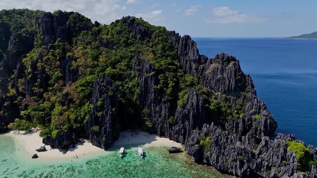 Wide drone flight moving backwards from Shimizu Island. Showcasing the majestic black limestone cliffs, turquoise lagoon and tropical beach in El Nido.