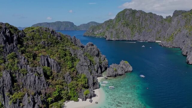 Cinematic drone flight from the ocean towards the beach, passing closely by sharp black limestone cliffs. Immersive tropical scenery in El Nido.