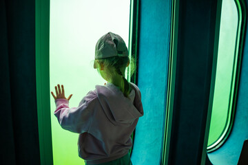 Little girl looking through underwater windows inside the diving gondola at Sellin Pier on Rugen island, Germany. Childhood curiosity and marine discovery concept. © dtatiana