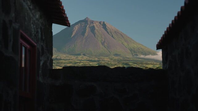 Cinematic View of Mount Pico Volcanic Cone Framed by Traditional Basalt Stone Houses at Sunset, Pico Island, Azores
