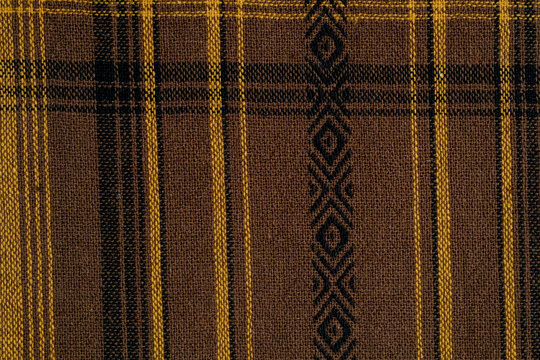 Brown fabric with plaid pattern and diamond motif Close up of brown fabric with woven yellow and black plaid and diamond details suitable for textile backgrounds