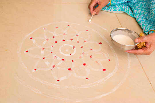 old lady hand making rangoli or alpana during vat savitri puja with rice paste and sindoor.
