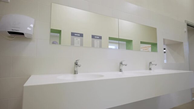 Row of ceramic sinks shows functional design along with cleanliness. Simple practical and organized view. Minimalist public toilet