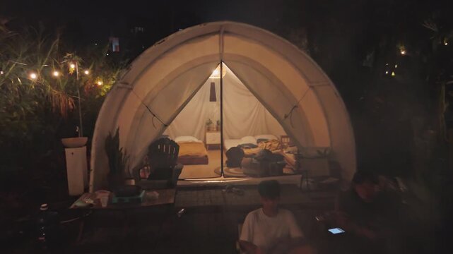 Cozy luxury glamping tent with warm interior lighting and friends gathered around campfire outside