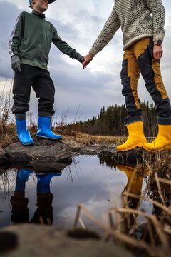 Adult and child holding hands on rocks with water reflection in nature