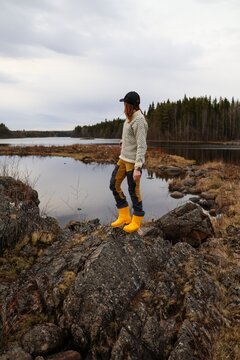 Woman standing on rocks by lake in Finnish nature wearing yellow boots