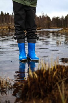 Child standing in shallow water wearing blue rubber boots in nature