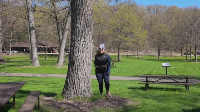 A woman jumps out from behind a tree in a joyful surprise in a park on a spring day.