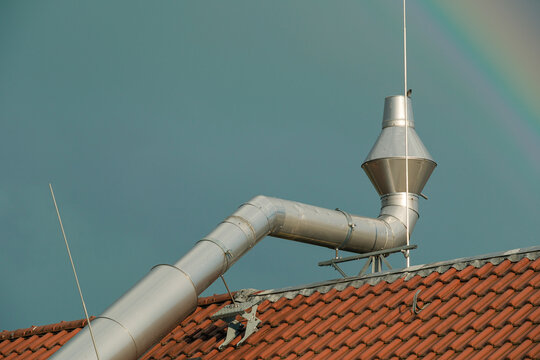 A bright rainbow over the roof with a ventilation pipe and red tiles. An urban architectural fragment against the background of a saturated sky.