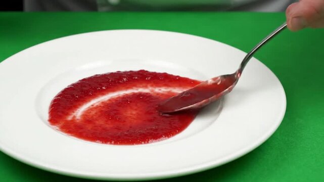Red jam spread white plate with spoon creating smooth swirl glossy texture vivid color evoking appetizing mood spoon ketchup plate hand sauce green background spoonful of ketchup white plate with