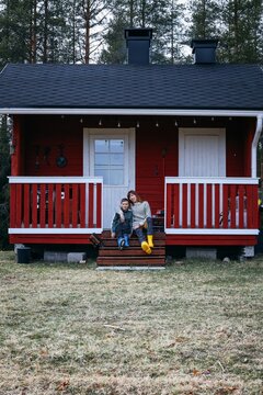 Mother and child sitting on porch of red wooden cabin in Finnish countryside