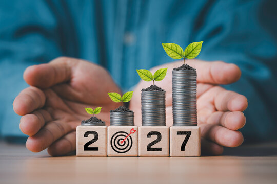Financial growth and investment planning concept with rising coin stacks and green plants protected by hands, symbolize wealth growth, savings, business success and sustainable finance target in 2027