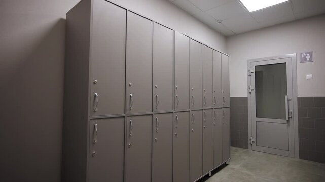 Minimalist locker room features row of clean grey cabinets. Spacious facility floor looks ready for changing and storage. Changing room