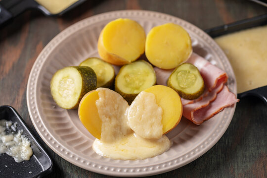 Delicious traditional Swiss melted raclette cheese on diced boiled or baked vegetables served in individual skillets