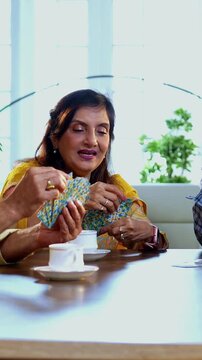 Indian senior adults playing cards game while seated at dining table in cozy modern home, laughing and bonding joyfully, Asian old aged friends celebrating cheerful indoor reunion with fun activity